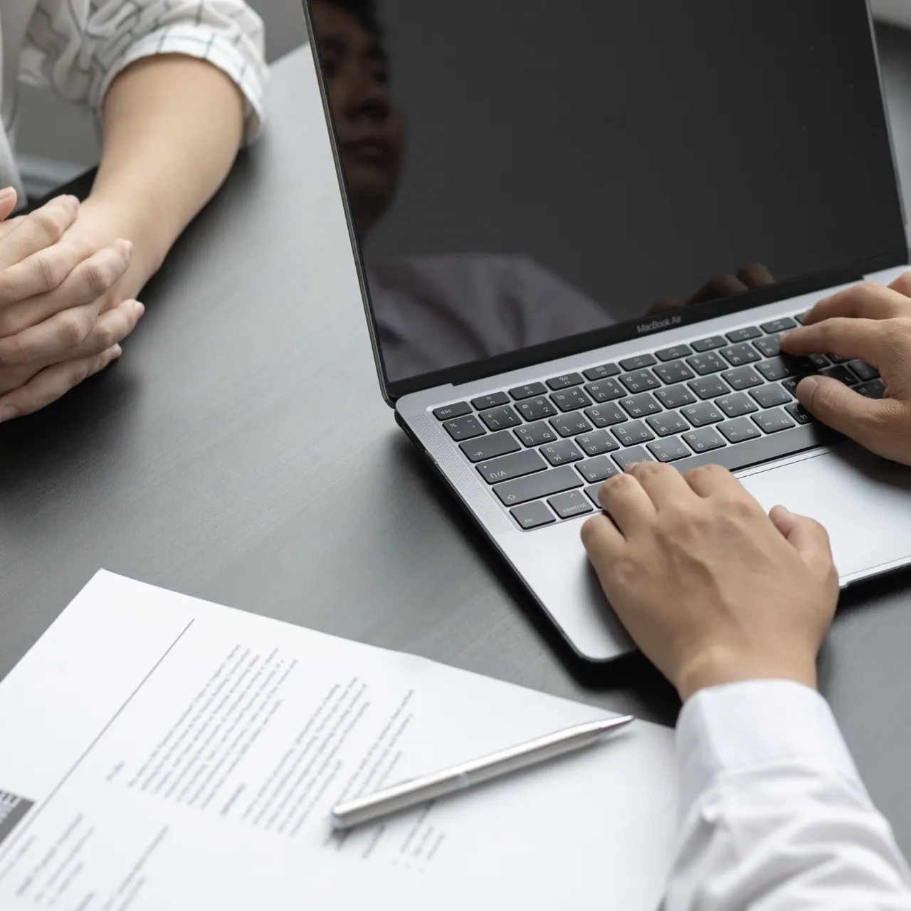Image personne devant son ordinateur avec un CV posé sur le bureau et une personne en face